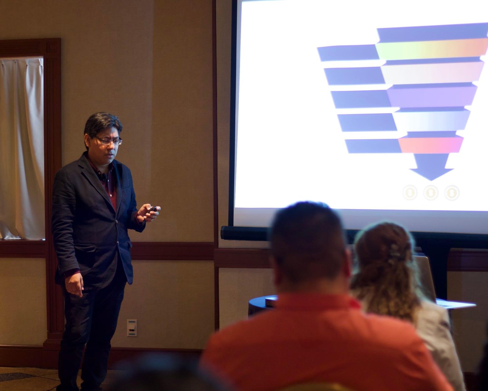 Yamil explaining a sales funnel on the screen of a hotel meeting room