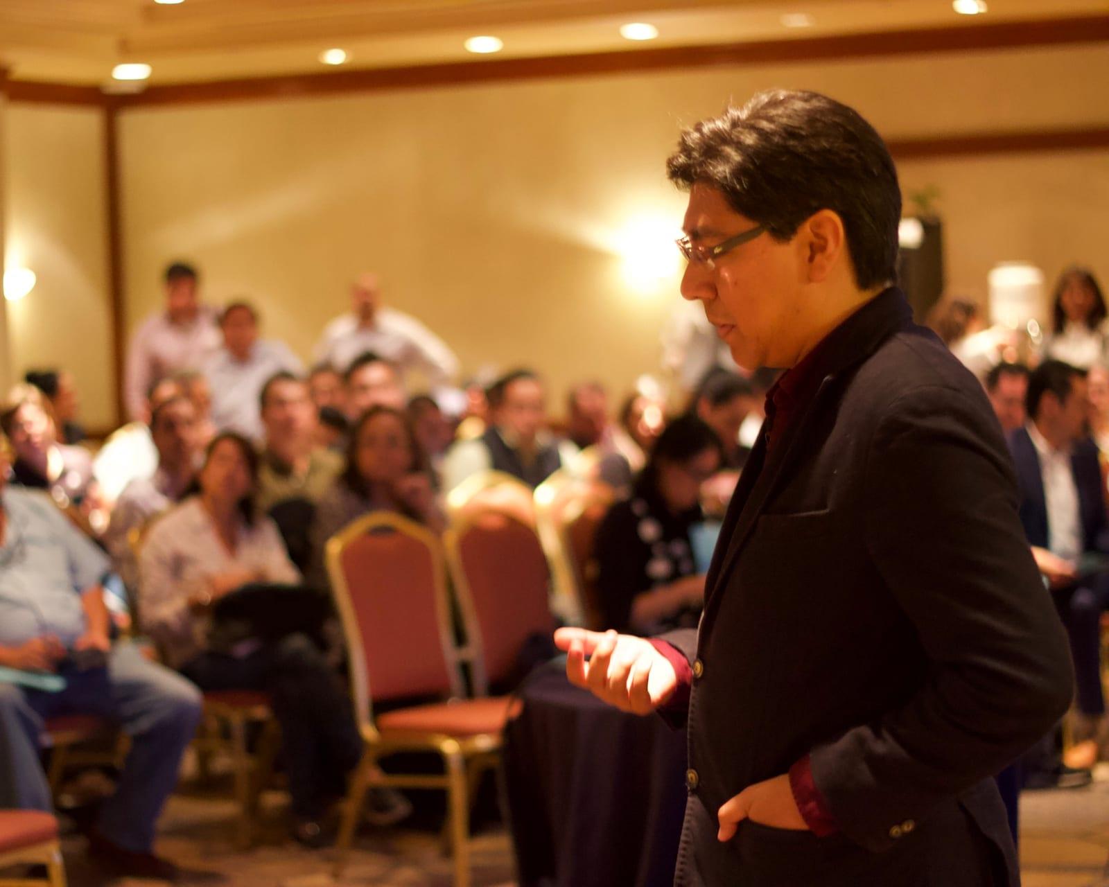 Yamil speaking to a full room, the audience out of focus behind him
