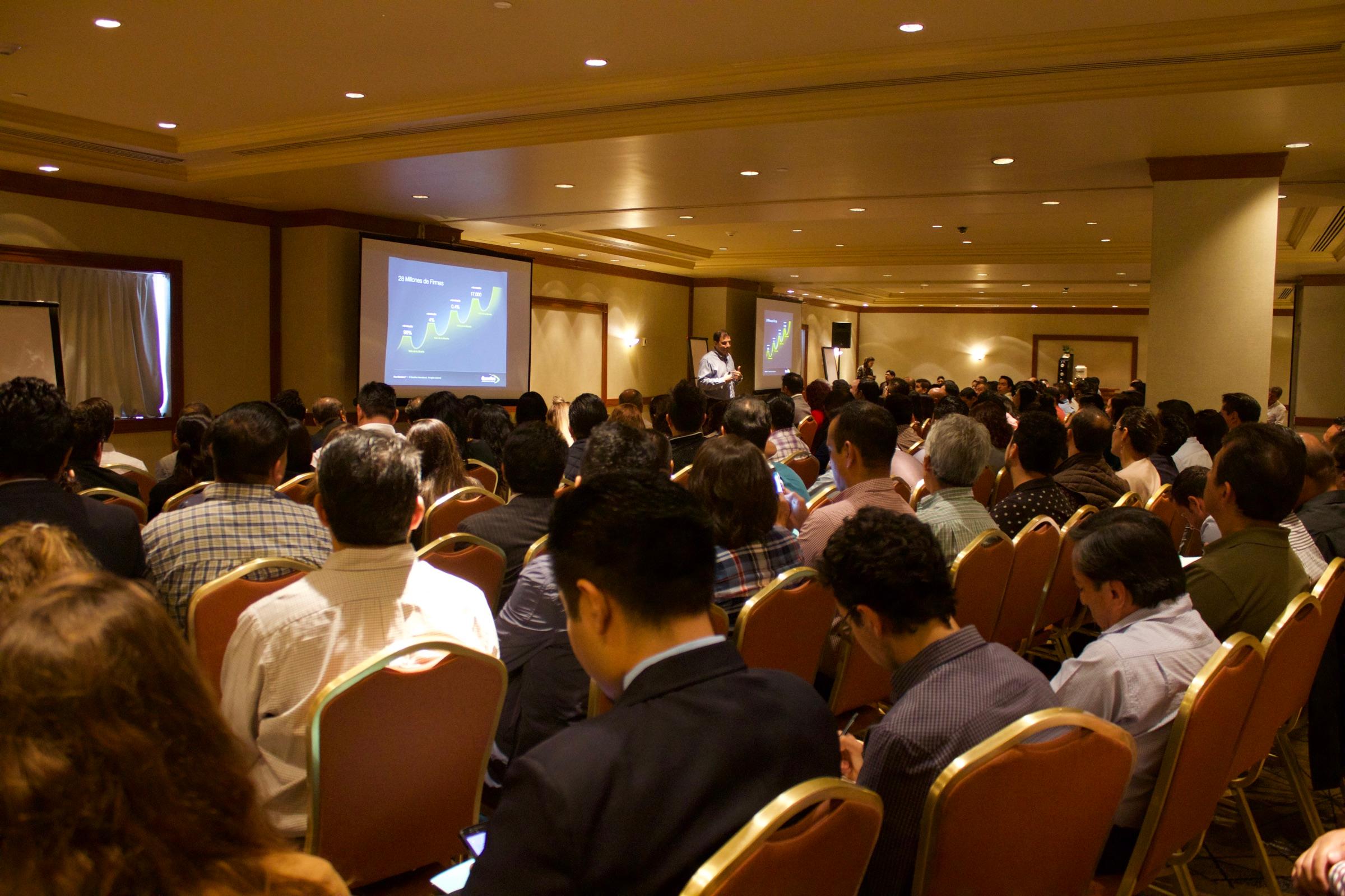 A full hotel ballroom listening to Yamil's presentation